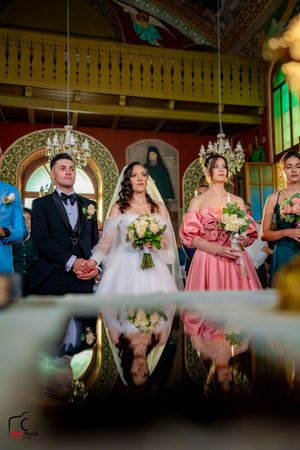 Mirror reflection captures wedding ceremony in ornate church with hanging chandeliers.