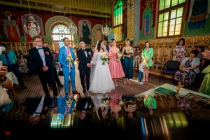 Wedding party stands in ornate church interior with colorful stained glass windows and reflective floor.