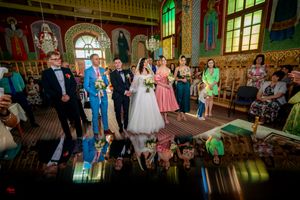Wedding group poses in ornate church with decorative walls and stained glass creating colorful reflections.