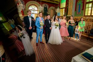 Formal wedding group photo in decorated church interior with painted walls and colored glass windows.
