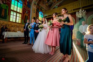Wedding party stands together in ornate church with colorful murals and stained glass lighting.