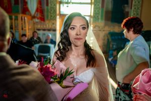 Close-up of bride holding pink and white floral bouquet in sunlit church interior.