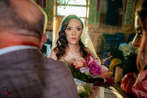 Bride in a white wedding dress looking down while holding a bouquet in an ornate church setting.