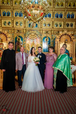 Large wedding party group photo in Orthodox church with golden iconostasis and striped flooring.