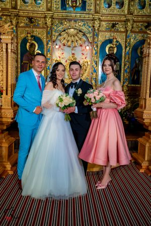 Wedding party in pink and blue attire pose for formal photos in front of church iconostasis.