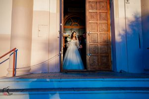Exterior view of church entrance with wooden doors and white walls against blue sky.