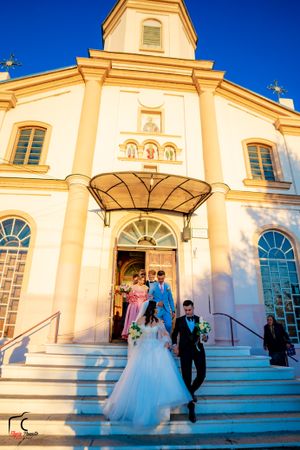 Wedding party poses on steps of cream-colored church during golden hour.