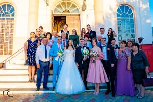 Large wedding group photo outside traditional church with arched windows and steps.