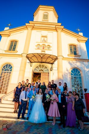 Wedding guests gather for group photos outside historic church with ornate facade.