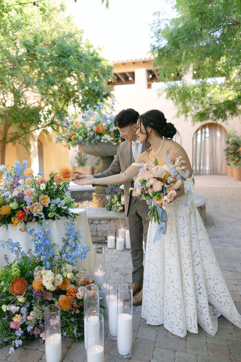 A couple stands by an elegant floral arrangement with white candles at a Spanish-style courtyard wedding venue.