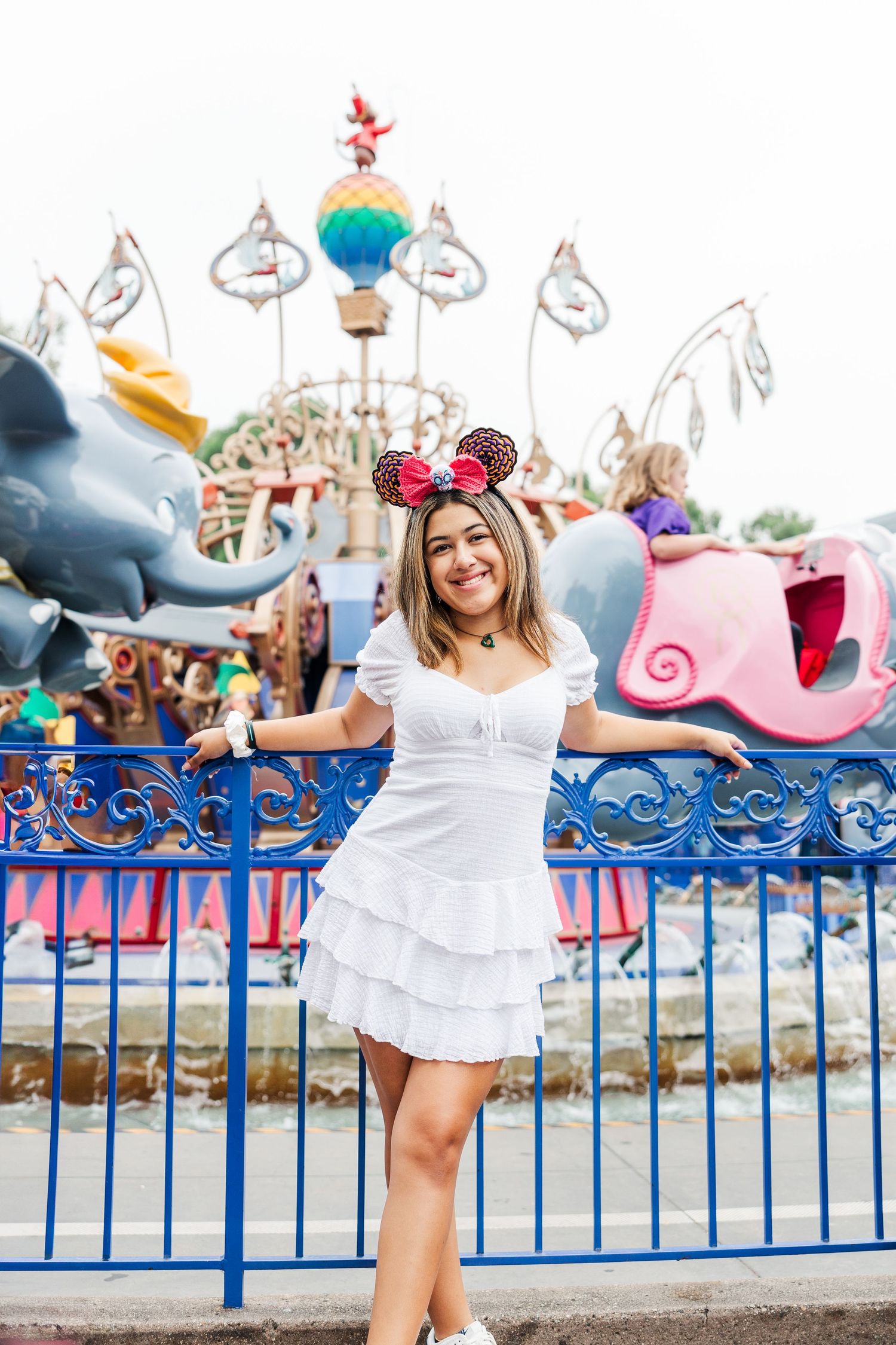 A white dress worn in front of a colorful amusement park ride with a blue fence and whimsical decorations.