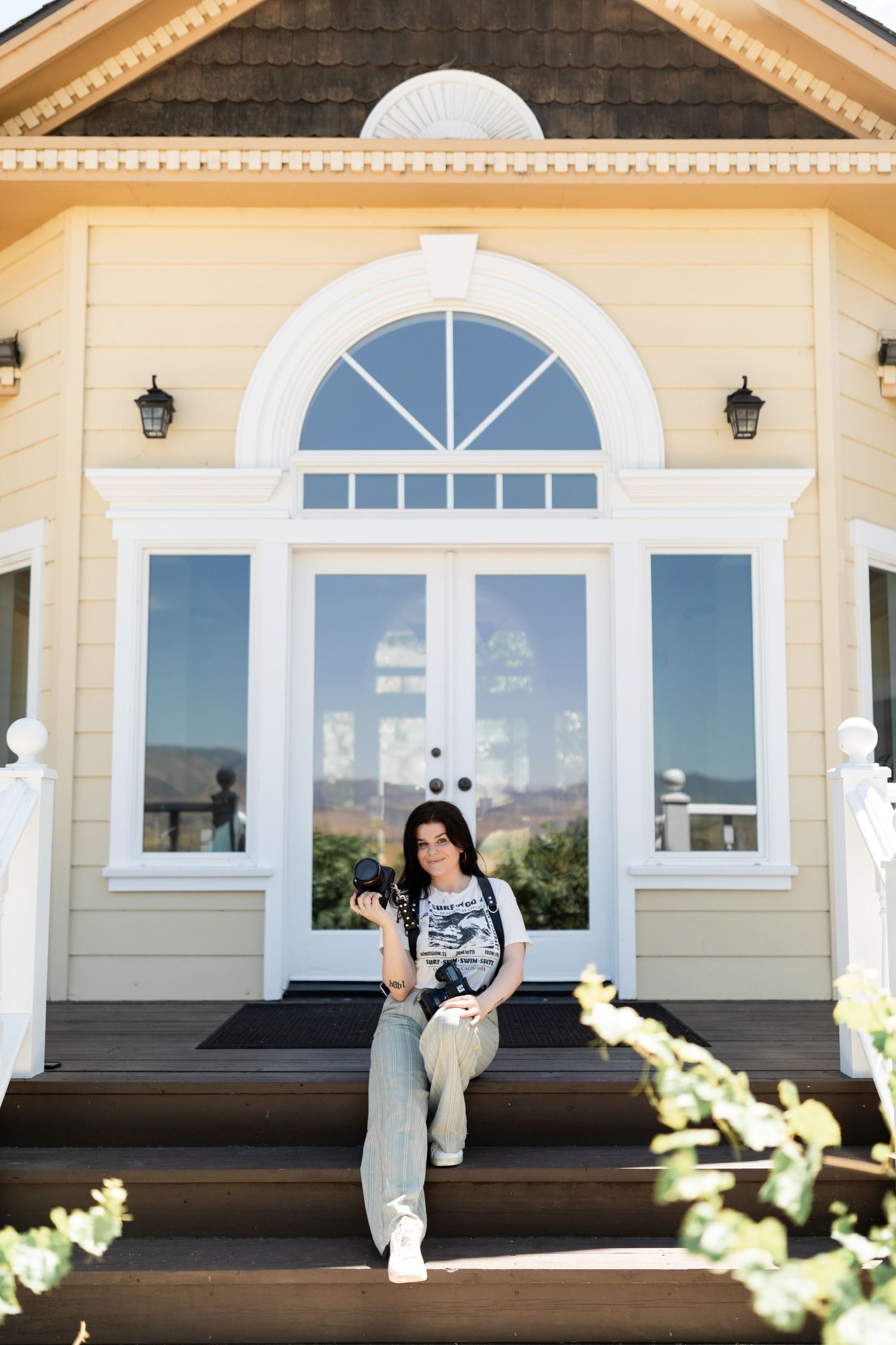 Elegant entrance of a cream-colored house with arched windows and decorative trim details with a photographer sitting on the steps.