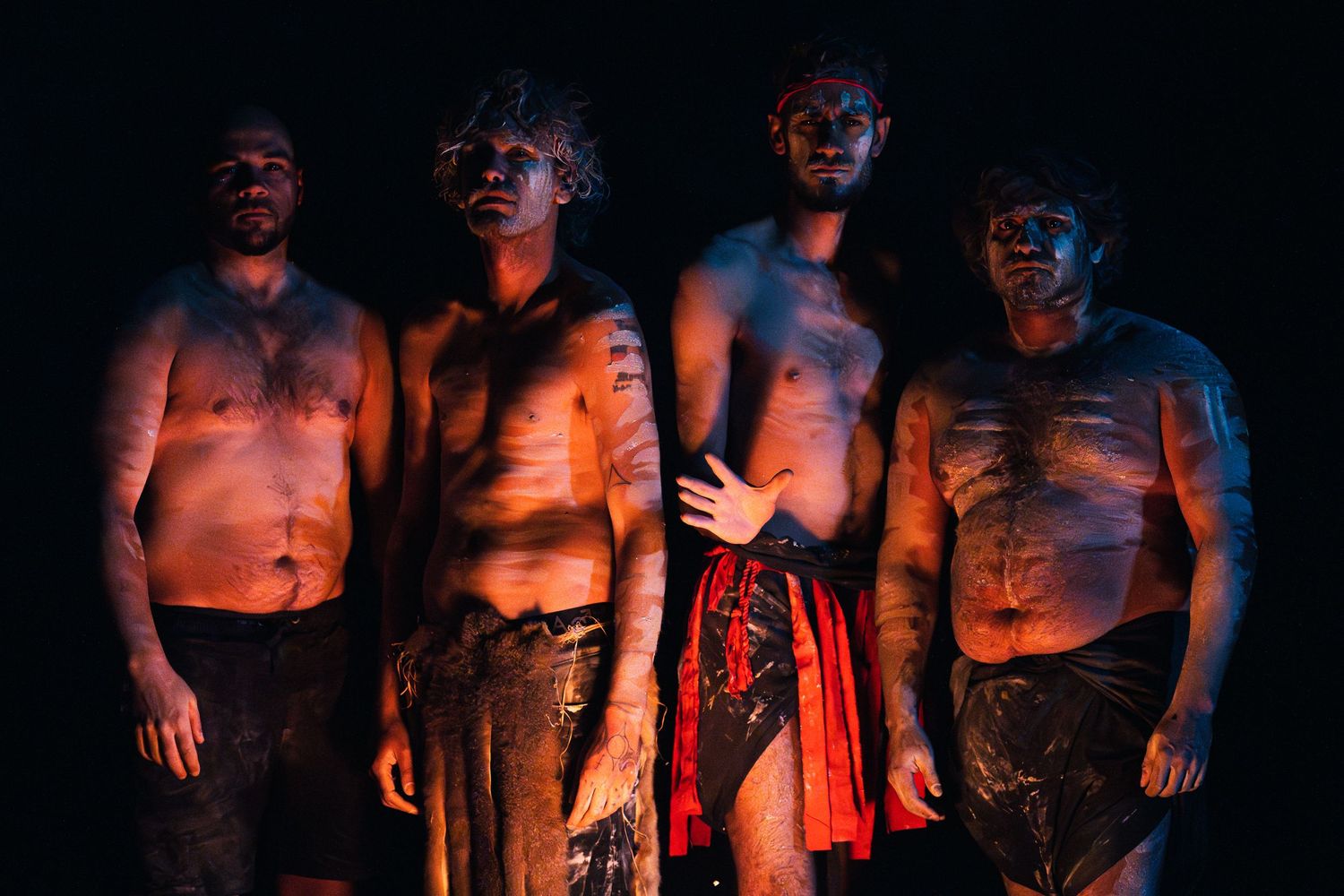 Group of shirtless figures illuminated by dramatic orange lighting in darkness.