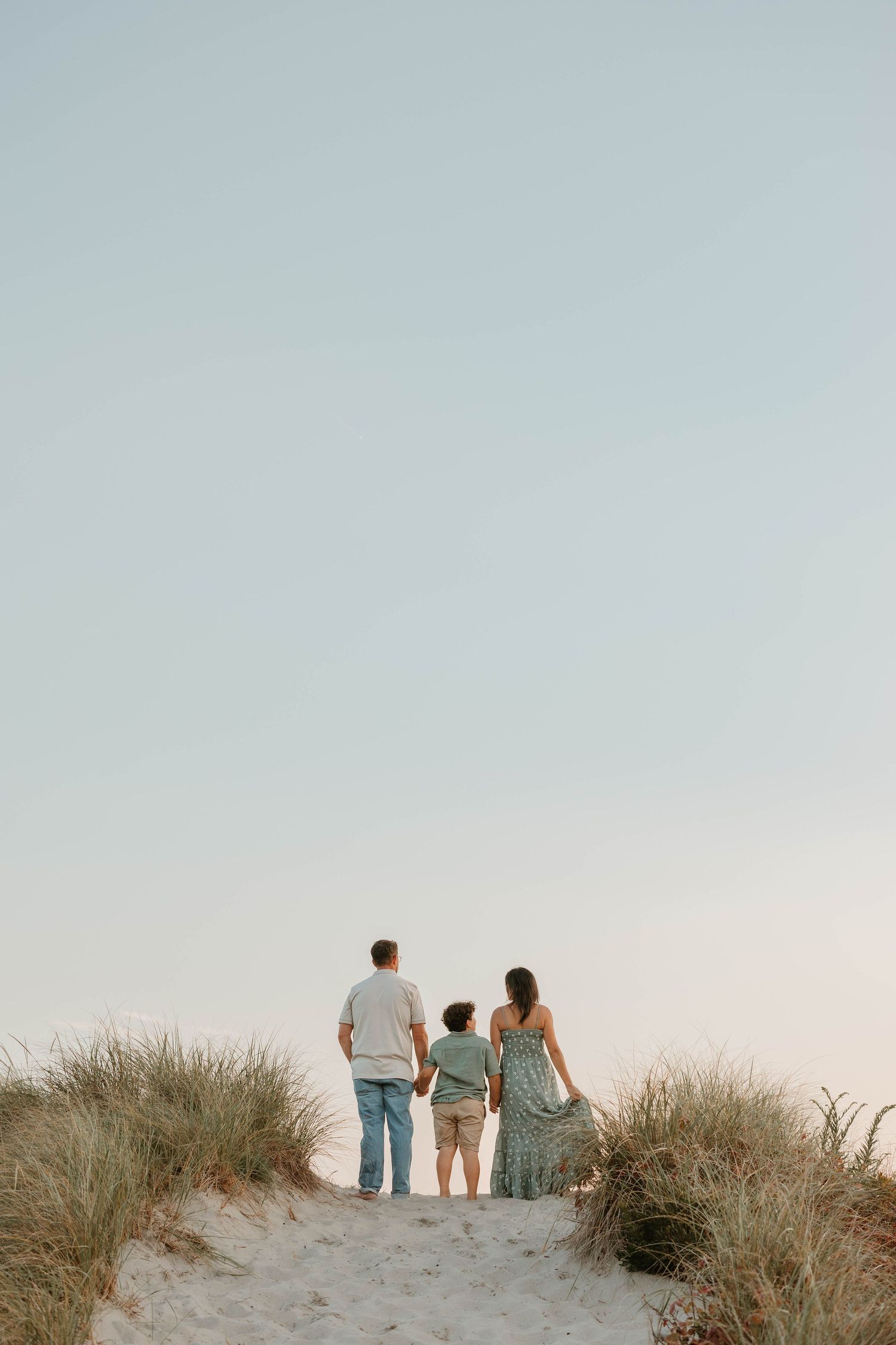 Three figures walking through coastal dunes at golden sunset.