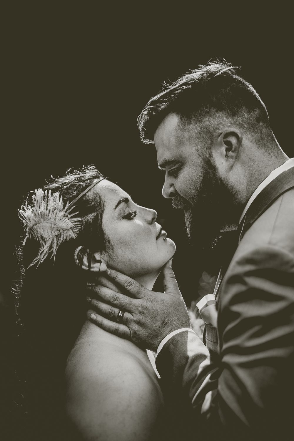 A dramatic black and white portrait of a couple in an intimate romantic moment, with rim lighting highlighting their silhouettes.