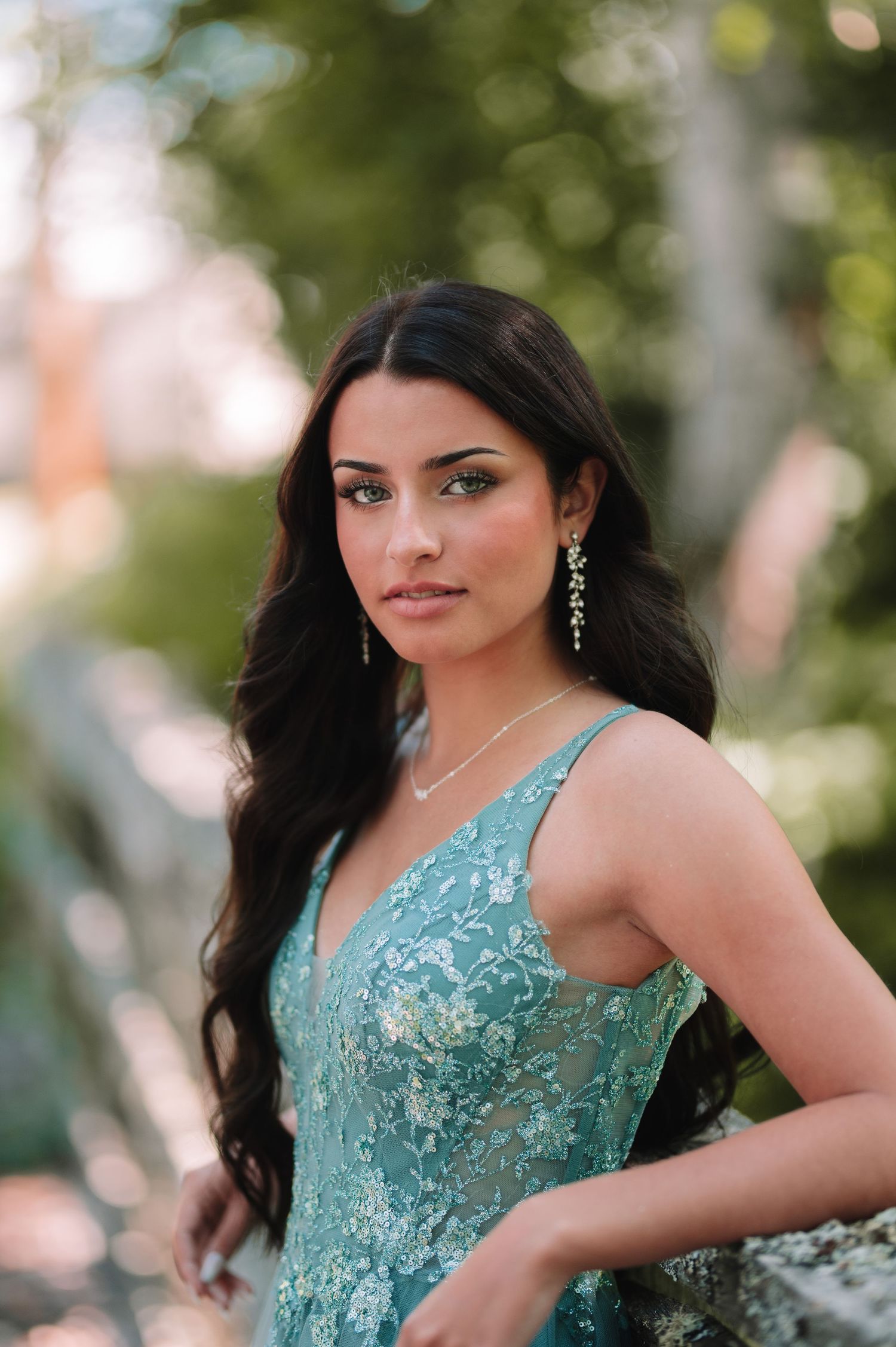 Woman in turquoise sequined formal gown poses in garden setting.
