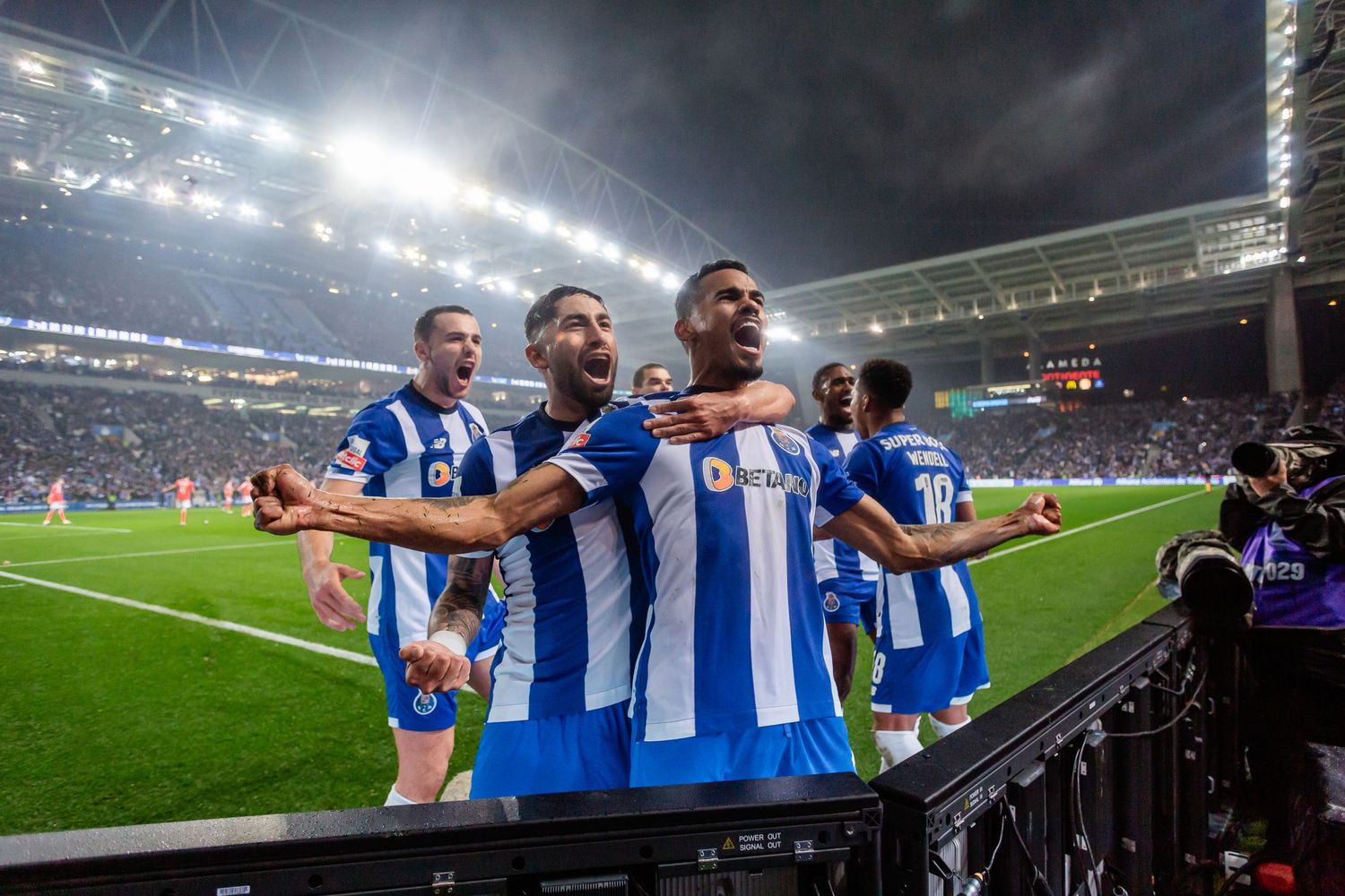 Soccer players celebrate on field during night game with stadium lights illuminating the scene.
