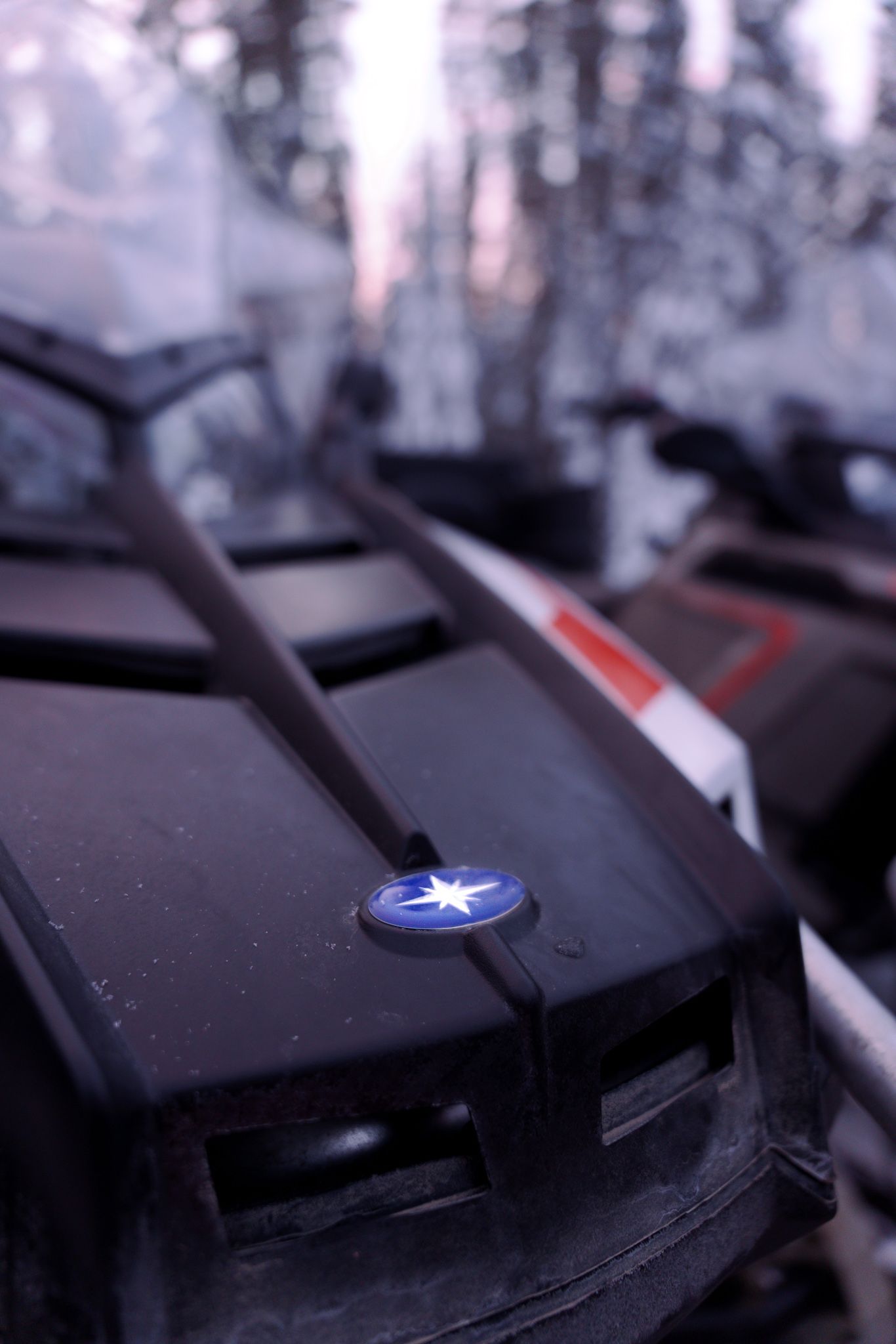 Close-up of a snowmobile ignition with a blue Polaris logo against a snowy winter backdrop.