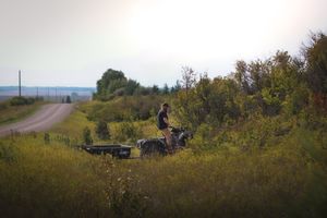 ATV rider traversing through tall grass on rural dirt path.