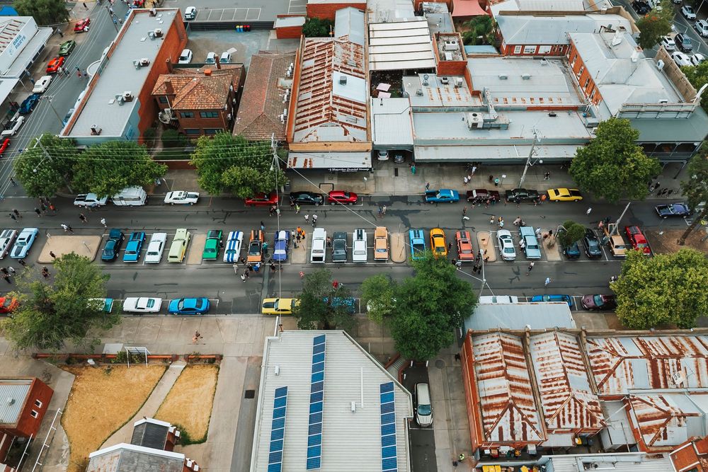 Aerial view of colorful parked cars in a city lot with rooftops and buildings visible from above.