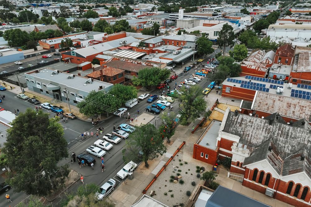 Aerial view of a small town with red rooftops, parked cars, and tree-lined streets in a residential area.
