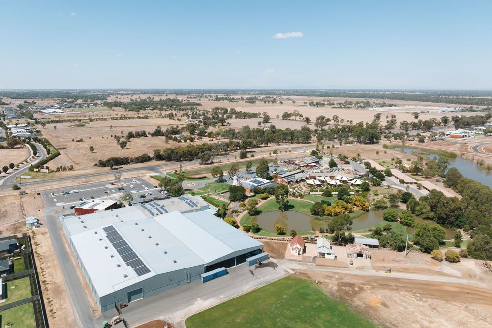 Aerial panoramic view of industrial buildings and warehouses in a rural area with dry landscape and scattered vegetation.