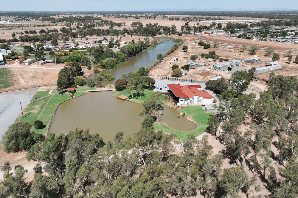 Aerial view of a residential area with red-roofed buildings near a winding river and green spaces in rural Australia.
