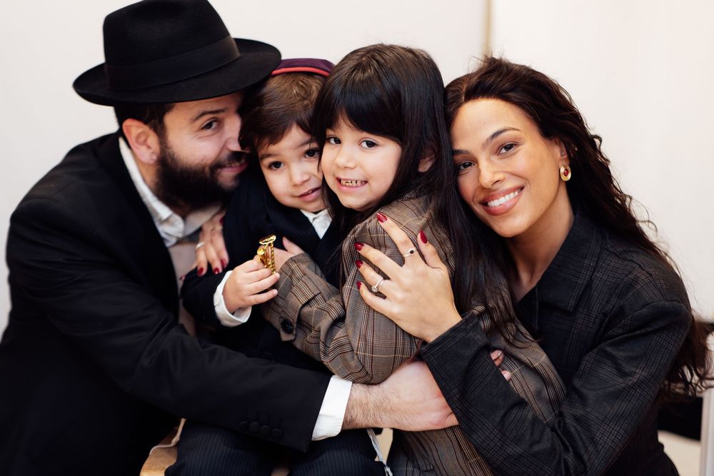 A joyful Jewish family with two young children smiling together at an indoor gathering.