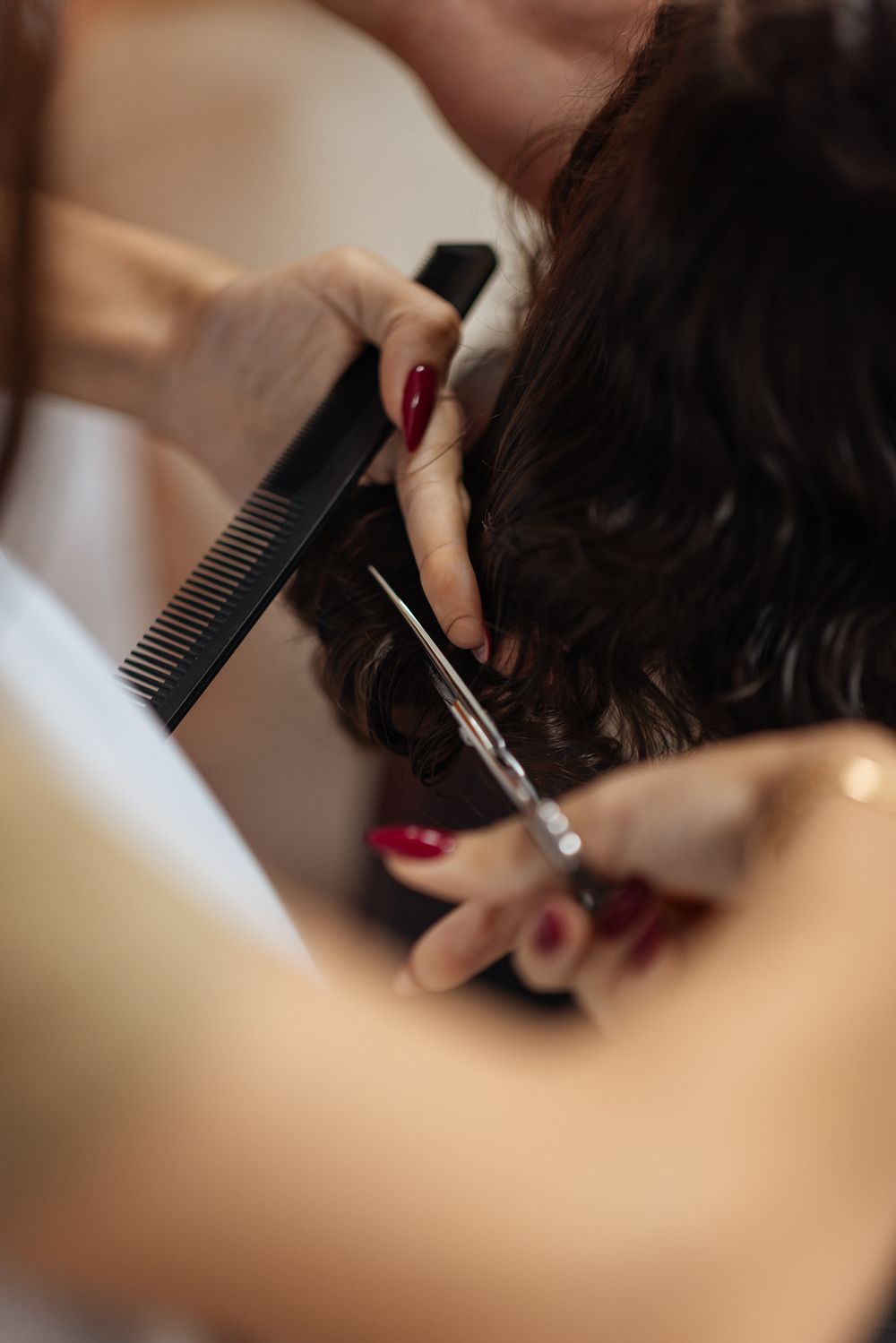Close-up shots of hairdressing scissors trimming dark hair with a black comb in a salon setting.