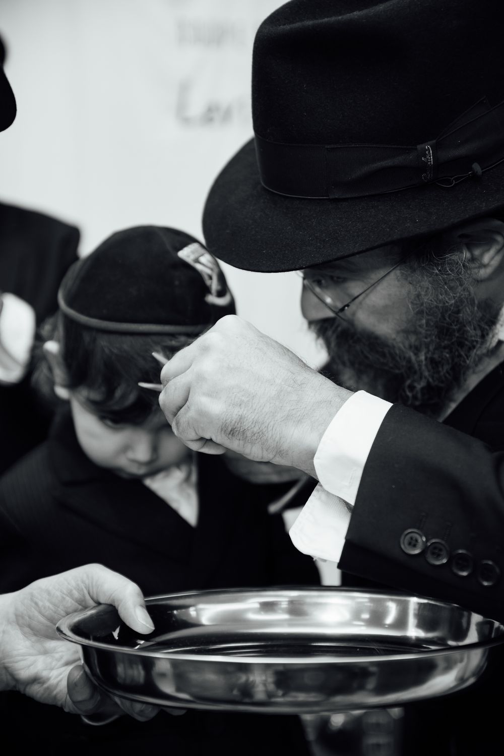 Orthodox Jewish rabbi performing a traditional Upsherin ceremony, cutting a young boy's hair over a silver plate.