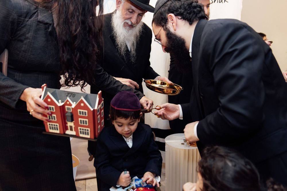 Jewish men and child examining a model building and dreidel at a Hanukkah celebration event.
