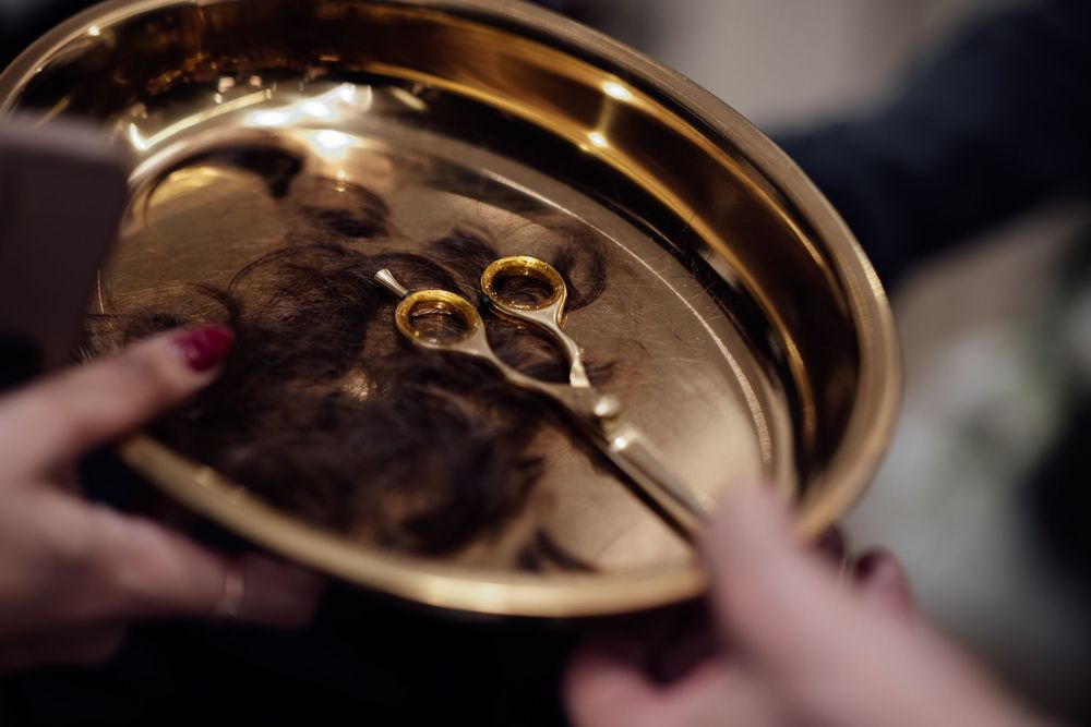 Close-up of two gold wedding rings on a golden ceremonial tray held by hands with red nail polish.