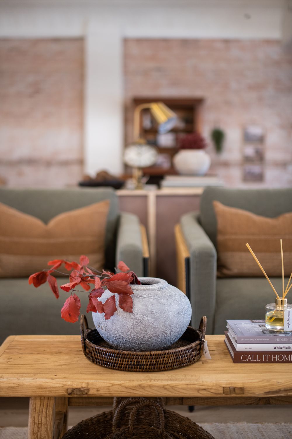 Wooden table displaying minimalist decor with ceramic vase and red foliage arrangement.