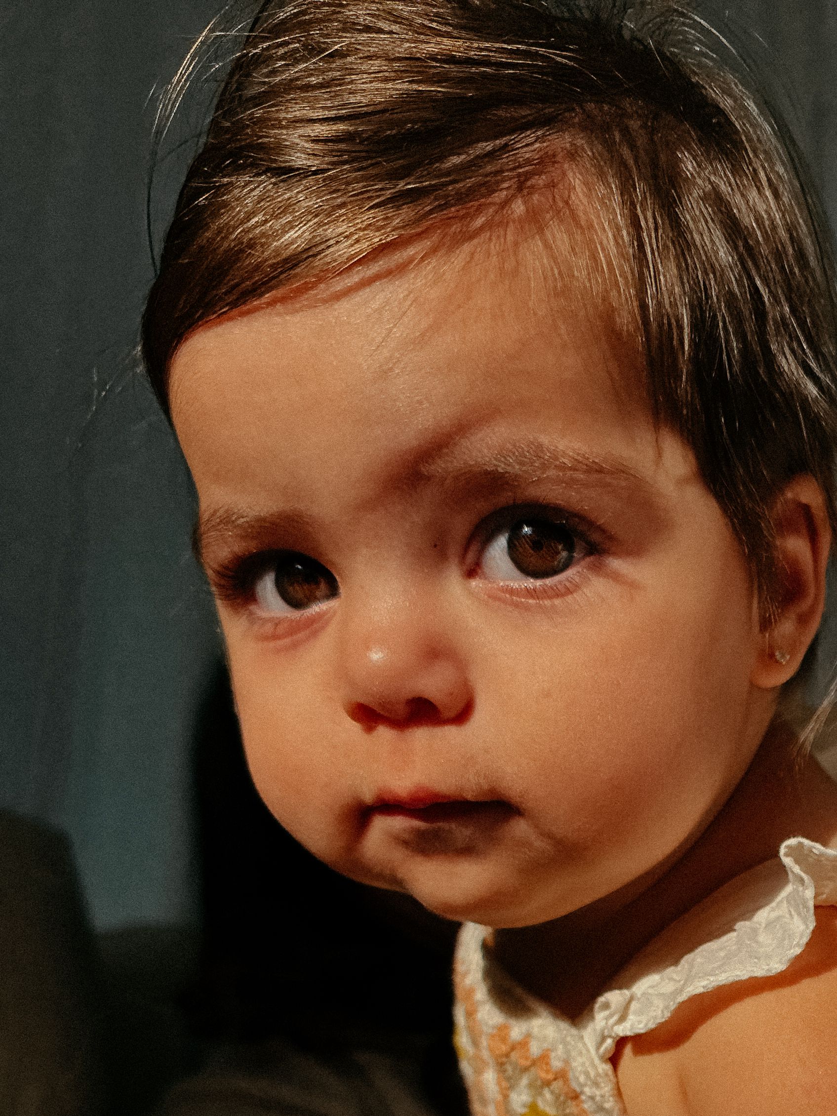 Close up portrait of a toddler in a lace dress looking to the side.