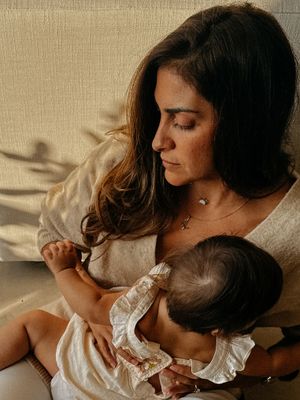 A brunette woman holds her baby while a shadow casts itself across her couch behind her