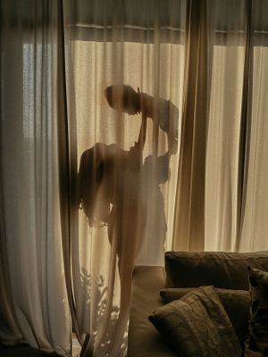 The silhouette of a woman holding her baby up in the air behind a pair of long white curtains