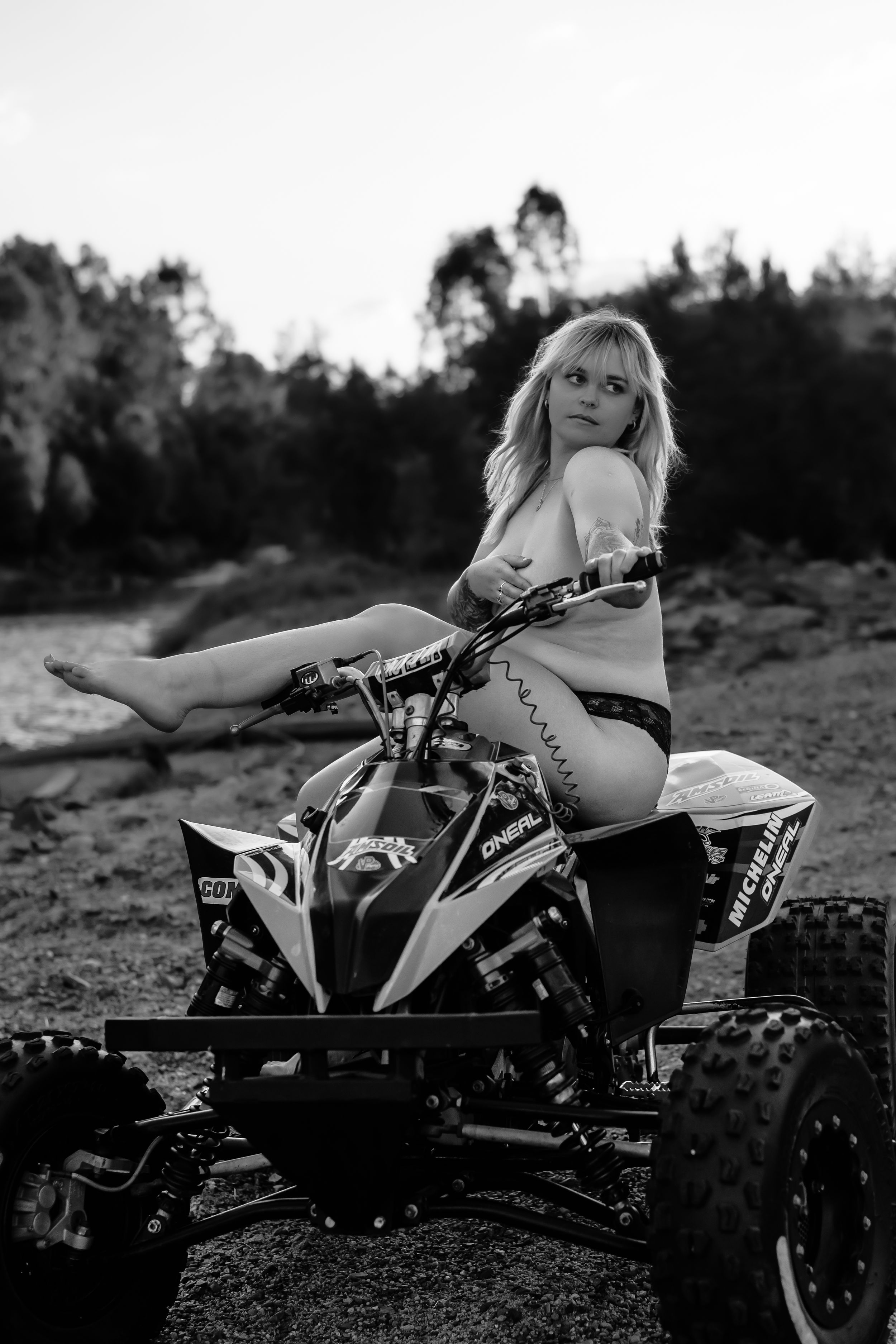 Black and white image of a person posed on an orange and black ATV quad bike against a natural backdrop.