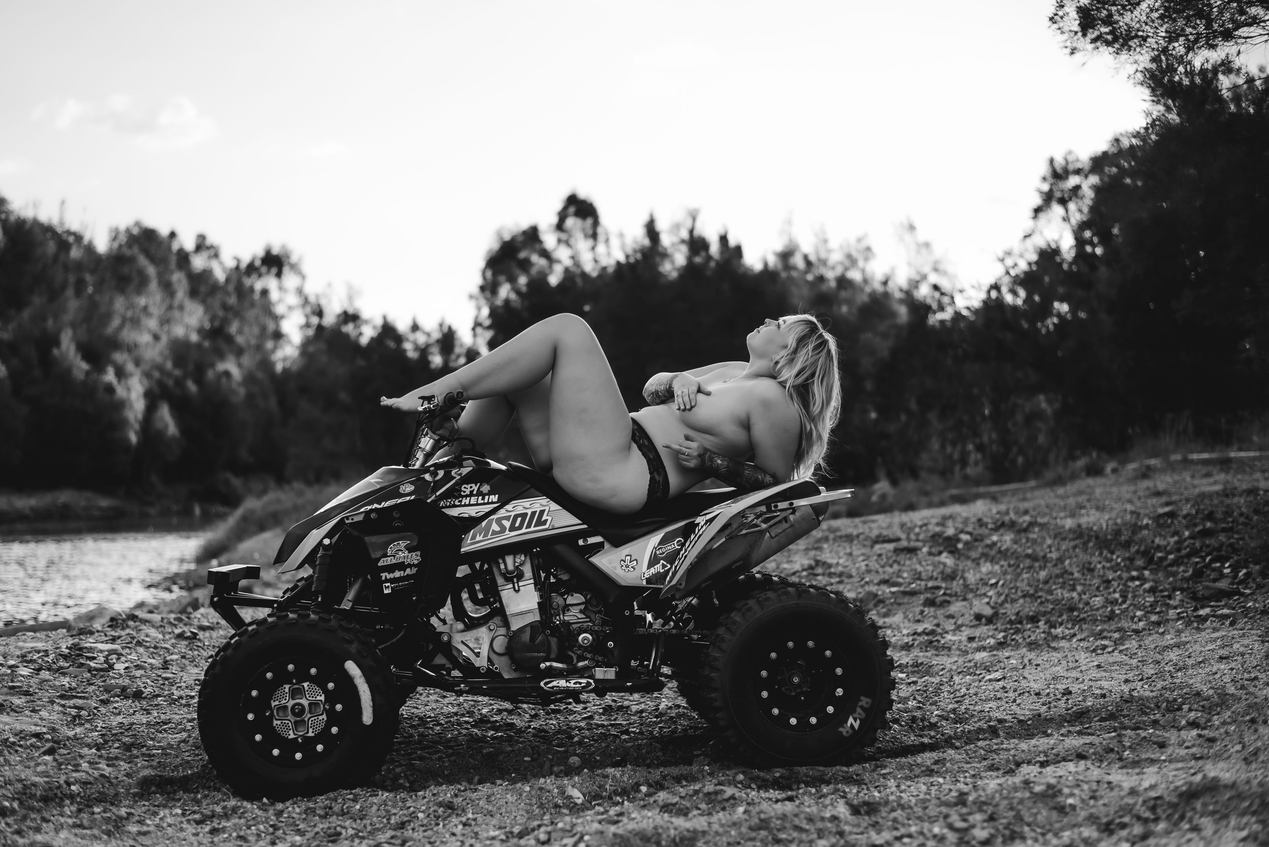 Monochrome photo of someone reclining on an ATV in an outdoor setting with trees in background.