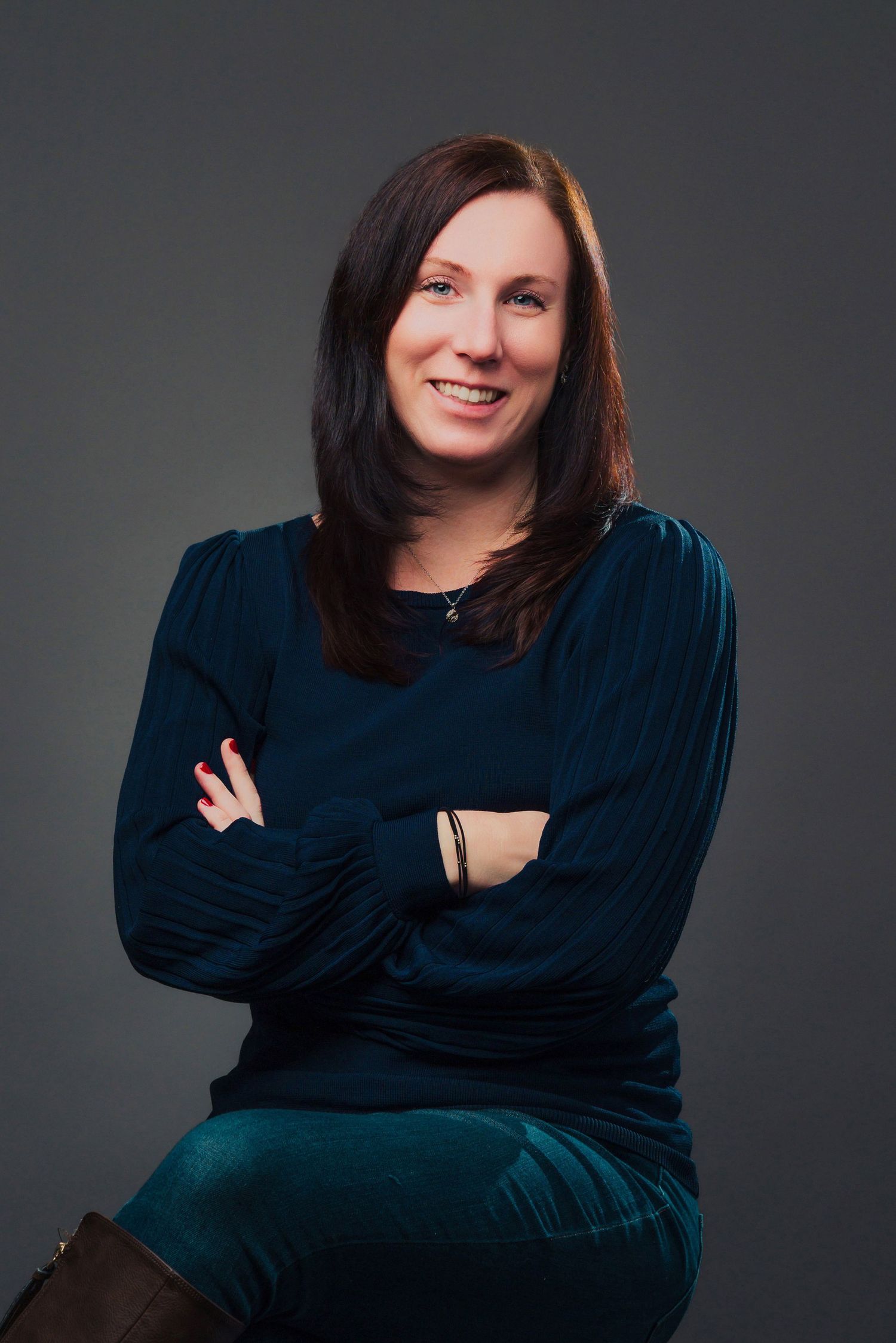 Professional portrait of a person in a navy blue sweater against a dark background.