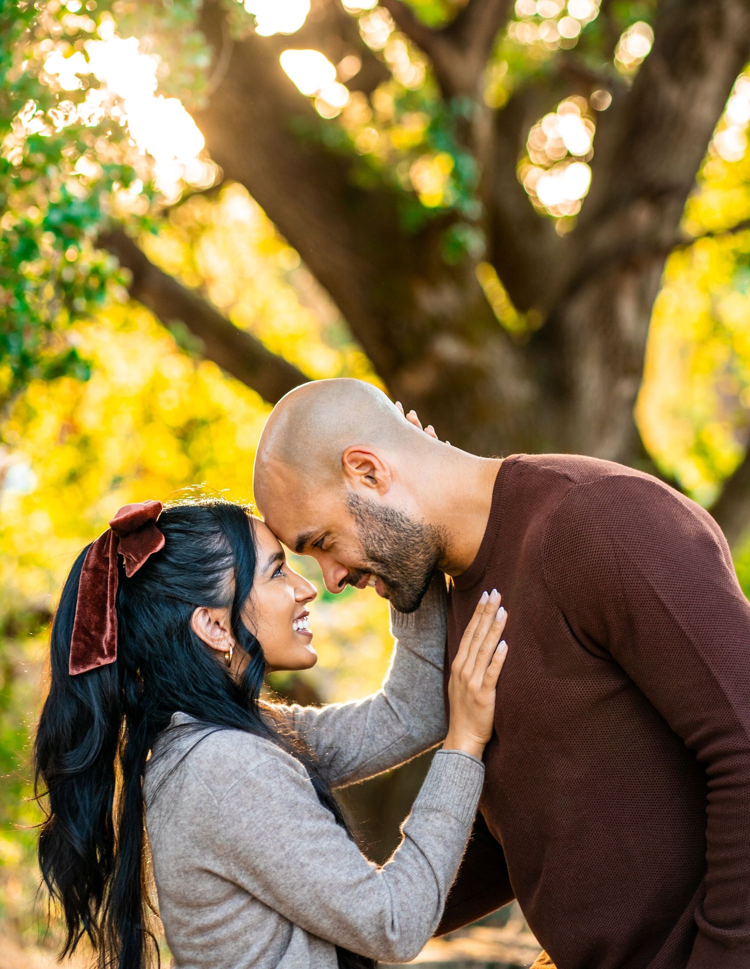 A couple shares a tender romantic moment against a sunlit backdrop of autumn trees and golden bokeh lighting.