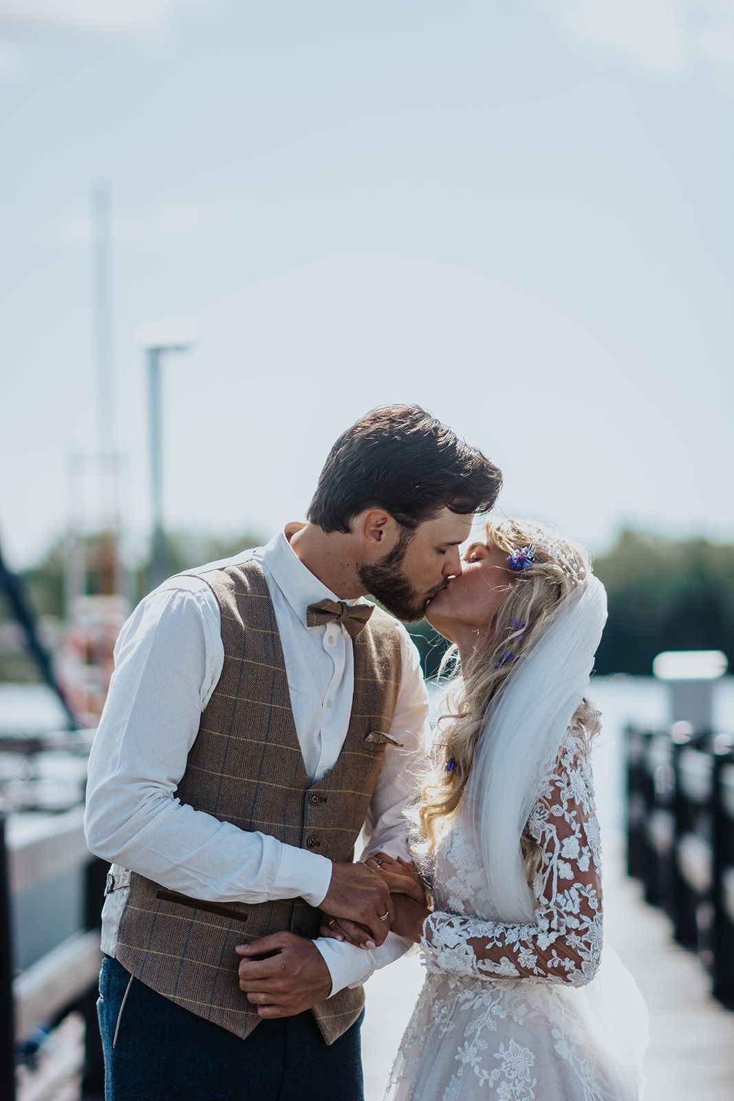 Romantic wedding couple sharing intimate moment on dock by water.