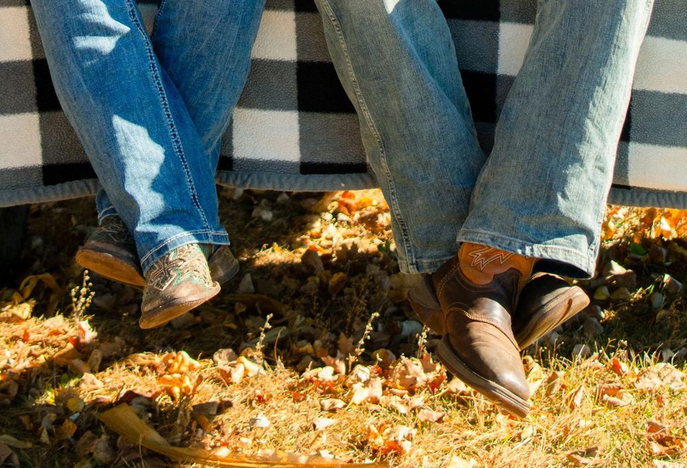 Girlfriend and boyfriend's western cowboys boots as they sit ankles crossed on a truck tailgate