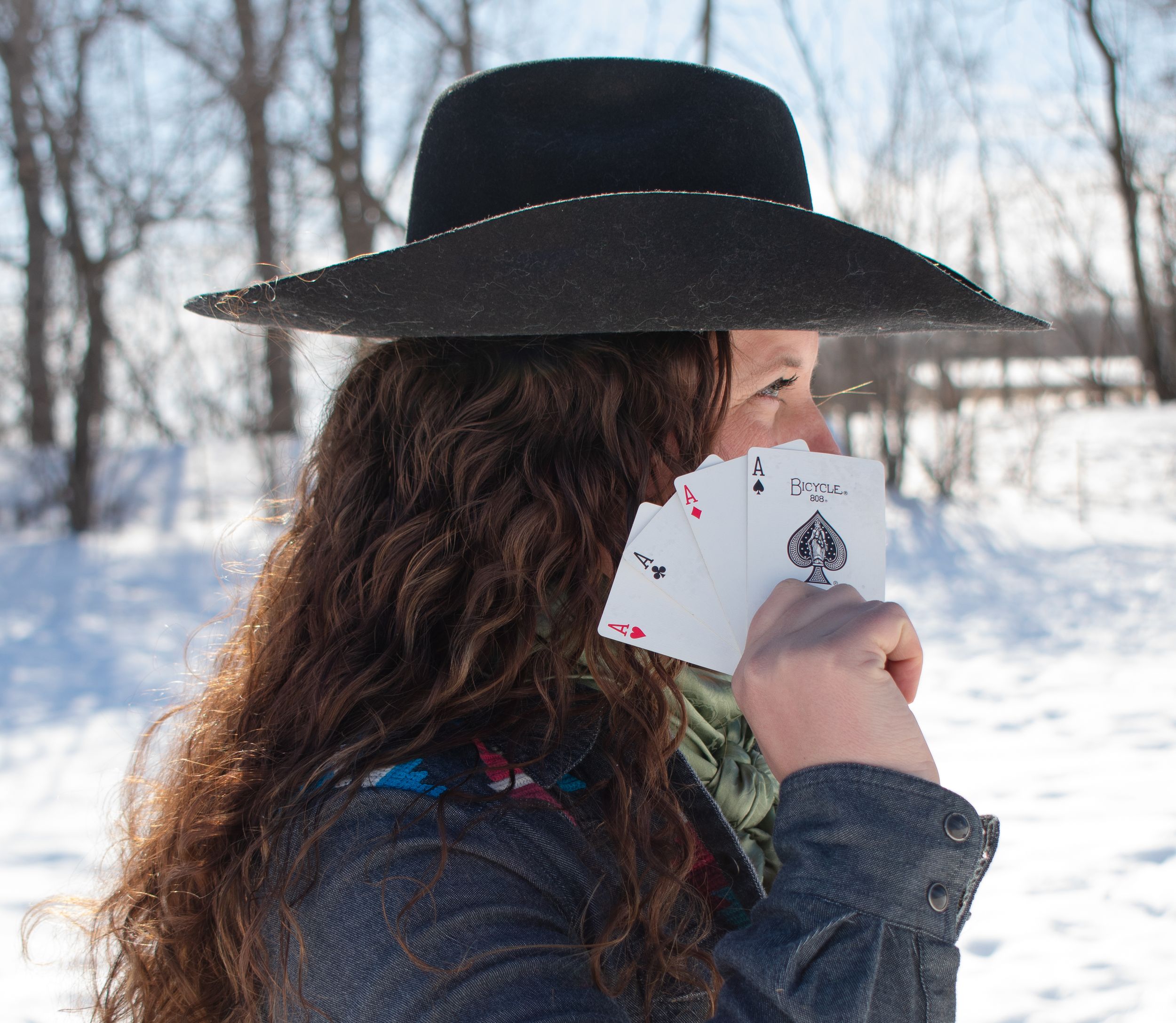 Cowgirl with 4 Ace Cards in front of face posed in a Wisconsin winter scene