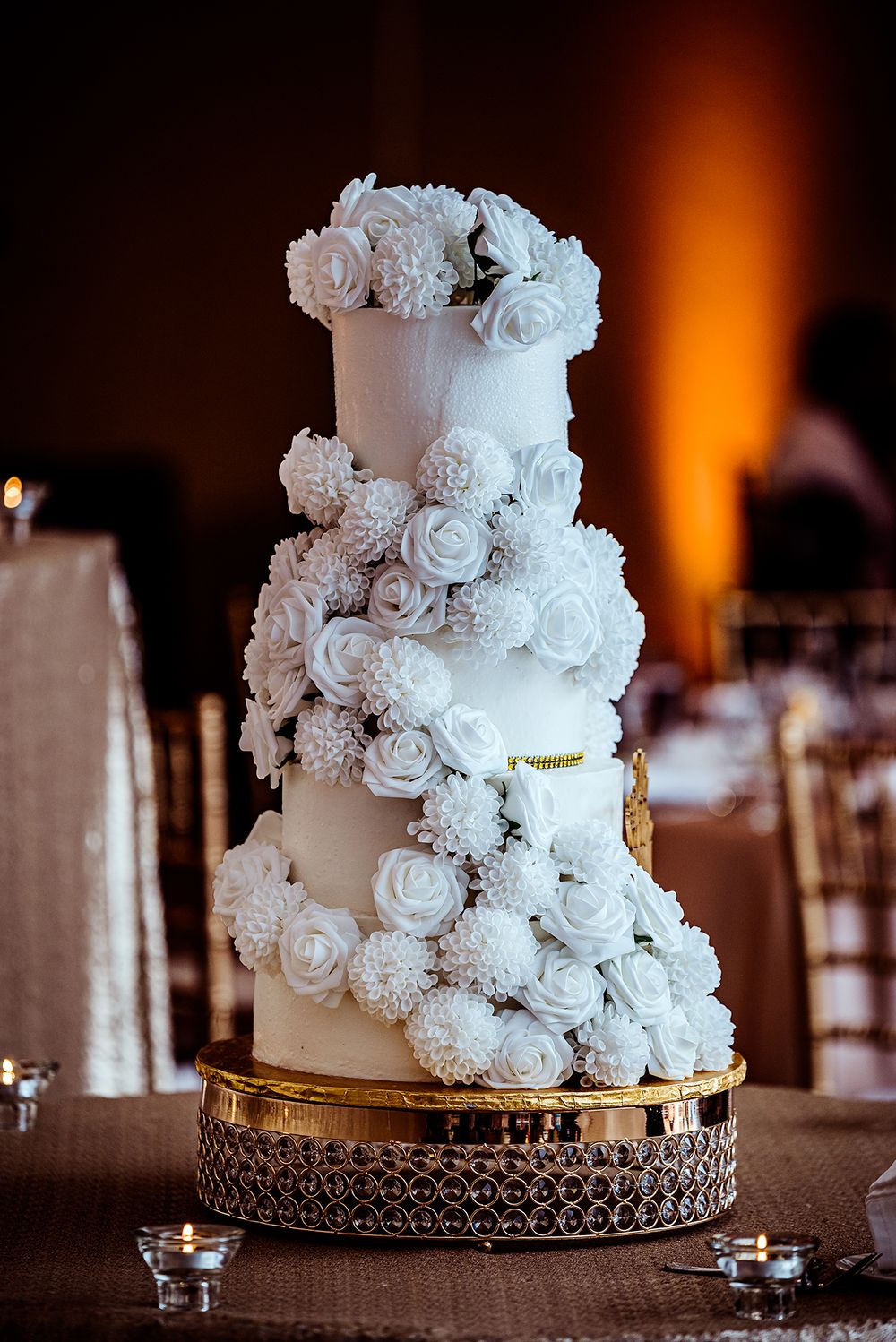 Four-tier white wedding cake decorated with cascading sugar roses on gold stand.