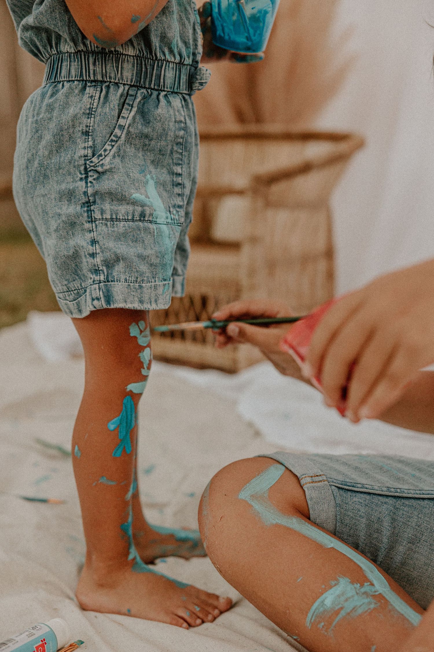 Someone painting blue decorative patterns on a leg wearing denim shorts.