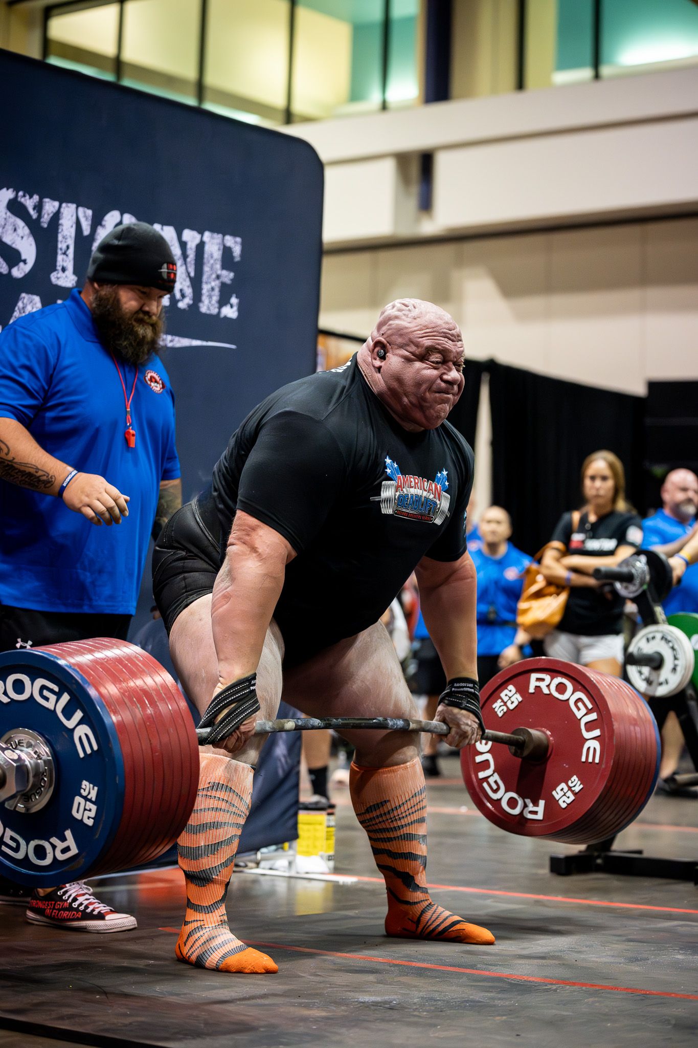 Strongman in orange striped socks performing heavy deadlift during competition event.