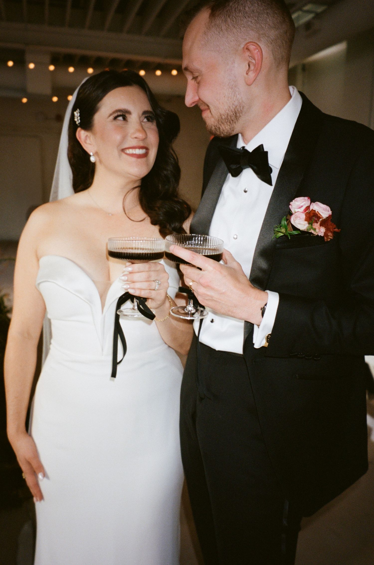 Newlyweds in formal attire share drinks and smiles during their wedding reception.