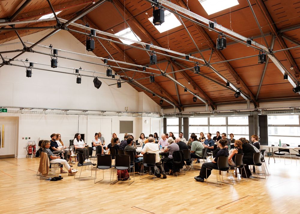 Large group of professionals gathered for a conference in a modern hall with wooden floors and vaulted ceiling.