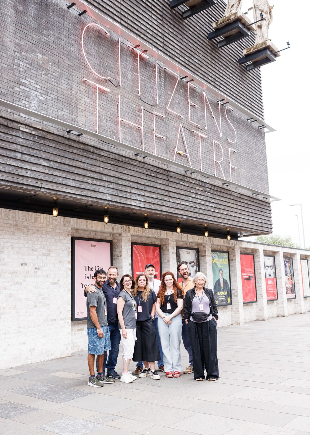Group of people posing outside Citizens Theatre, Glasgow, a iconic brick building with neon signage.