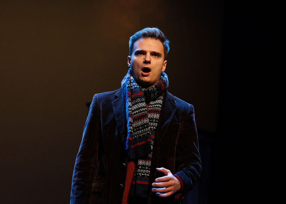 A performer in a dark suit sings passionately on stage under dramatic blue lighting during a concert performance.